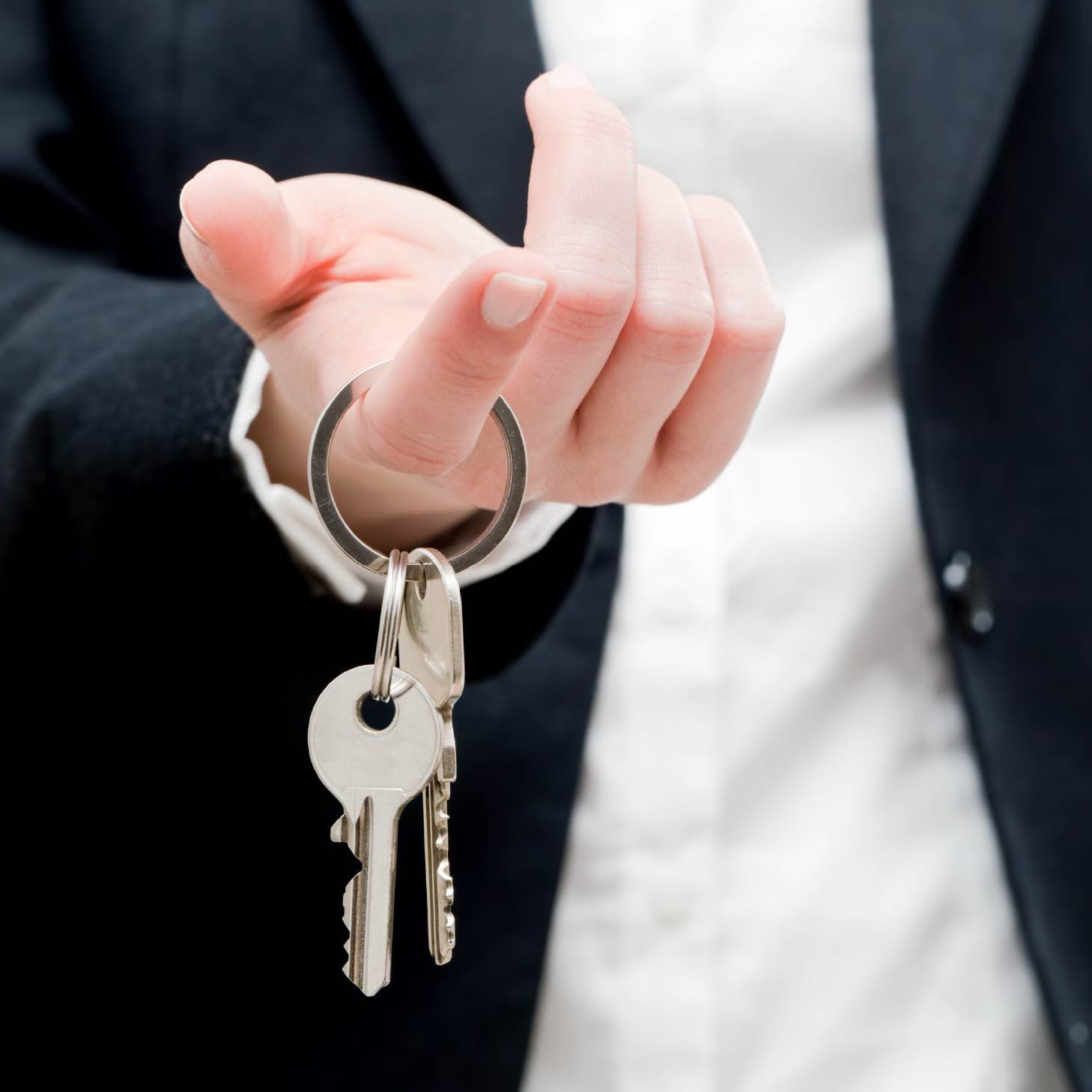Person in a suit holding a set of keys on a keyring, offering them forward.