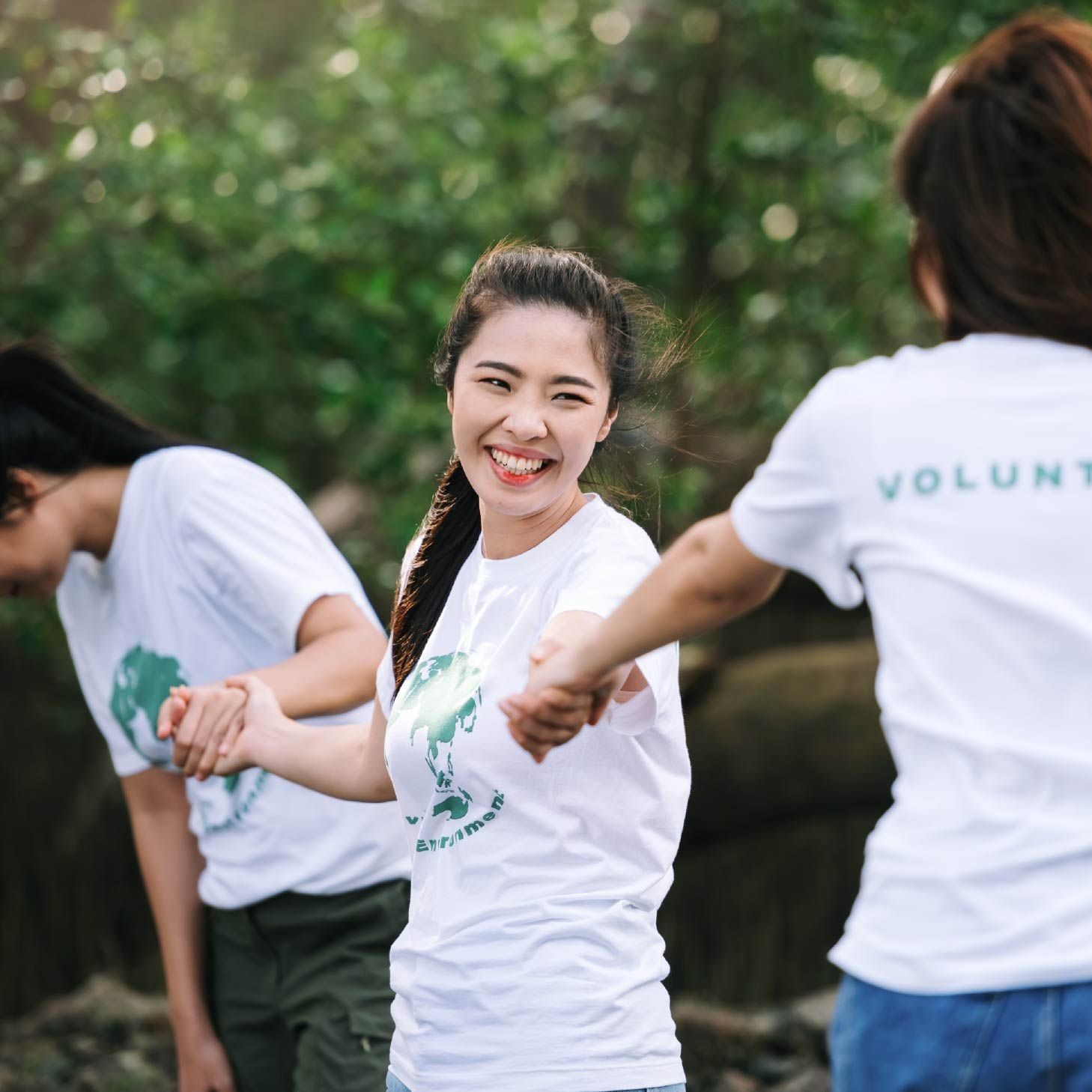 Group of smiling volunteers in environmental T-shirts holding hands outdoors.